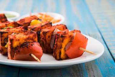 Paneer Tikka Kabab - Hint Tandoori peynir şişleri, malai paneer tikka / biber paneer malai paneer kabab, servis beyaz tabak Barbekü sopa ve renkli kırmızı biber ve soğan, yeşil sos ile