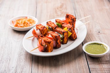 Paneer Tikka Kabab - Tandoori Indian cheese skewers, malai paneer tikka / malai paneer kabab, chilli paneer served in white plate with barbecue stick and colourful capsicum and onion, with green sauce clipart
