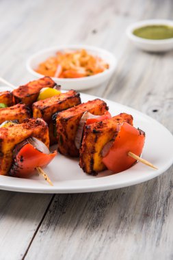 Paneer Tikka Kabab - Hint Tandoori peynir şişleri, malai paneer tikka / biber paneer malai paneer kabab, servis beyaz tabak Barbekü sopa ve renkli kırmızı biber ve soğan, yeşil sos ile