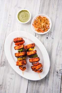 Paneer Tikka Kabab - Hint Tandoori peynir şişleri, malai paneer tikka / biber paneer malai paneer kabab, servis beyaz tabak Barbekü sopa ve renkli kırmızı biber ve soğan, yeşil sos ile