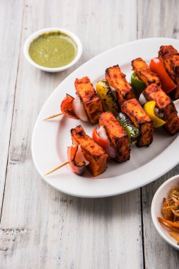 Paneer Tikka Kabab - Hint Tandoori peynir şişleri, malai paneer tikka / biber paneer malai paneer kabab, servis beyaz tabak Barbekü sopa ve renkli kırmızı biber ve soğan, yeşil sos ile