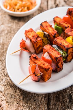 Paneer Tikka Kabab - Hint Tandoori peynir şişleri, malai paneer tikka / biber paneer malai paneer kabab, servis beyaz tabak Barbekü sopa ve renkli kırmızı biber ve soğan, yeşil sos ile