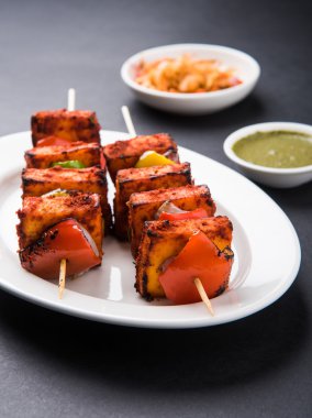 Paneer Tikka Kabab - Hint Tandoori peynir şişleri, malai paneer tikka / biber paneer malai paneer kabab, servis beyaz tabak Barbekü sopa ve renkli kırmızı biber ve soğan, yeşil sos ile