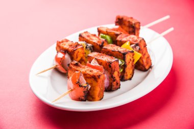 Paneer Tikka Kabab - Hint Tandoori peynir şişleri, malai paneer tikka / biber paneer malai paneer kabab, servis beyaz tabak Barbekü sopa ve renkli kırmızı biber ve soğan, yeşil sos ile