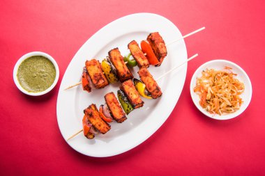 Paneer Tikka Kabab - Hint Tandoori peynir şişleri, malai paneer tikka / biber paneer malai paneer kabab, servis beyaz tabak Barbekü sopa ve renkli kırmızı biber ve soğan, yeşil sos ile