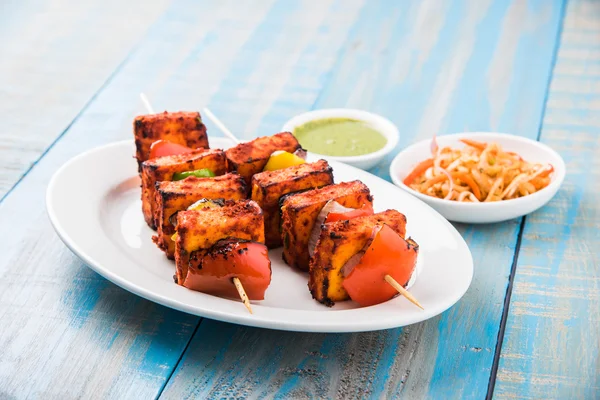 Paneer Tikka Kabab - Tandoori Indian cheese skewers, malai paneer tikka / malai paneer kabab, chilli paneer served in white plate with barbecue stick and colourful capsicum and onion, with green sauce — Stock Photo, Image