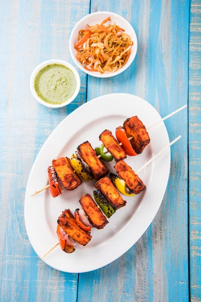 Paneer Tikka Kabab - индийские сырные шашлыки тандури, малай панир тикка / малай панир кабаб, чили панир подается в белой тарелке с палочкой для барбекю и красочный капсикум и лук, с зеленым соусом — стоковое фото