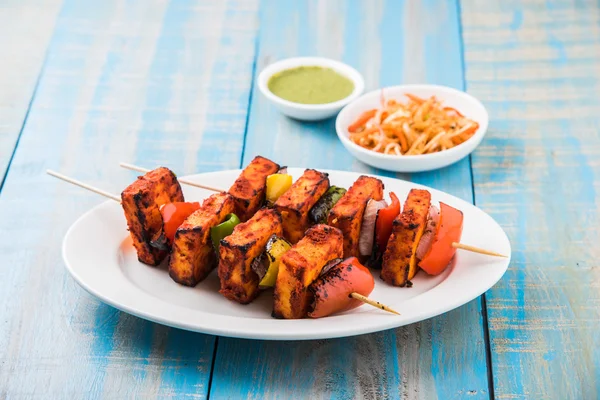 Paneer Tikka Kabab - Tandoori Indian cheese skewers, malai paneer tikka / malai paneer kabab, chilli paneer served in white plate with barbecue stick and colourful capsicum and onion, with green sauce — Stock Photo, Image