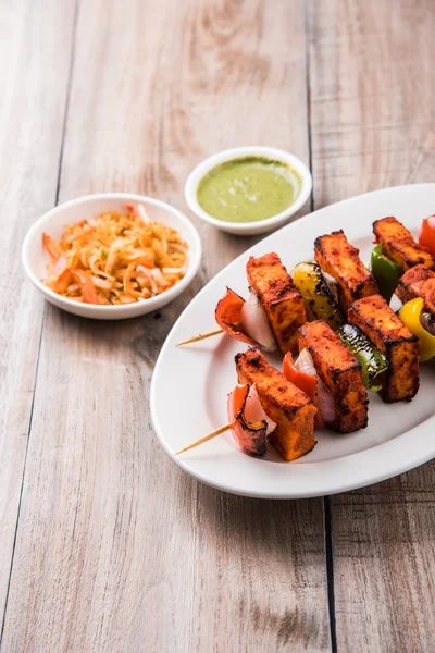 Paneer Tikka Kabab - Brochettes de fromage indien Tandoori, paneer malai tikka / malai paneer kabab, paneer de piment servi dans une assiette blanche avec bâton de barbecue et capsicum coloré et oignon, avec sauce verte — Photo