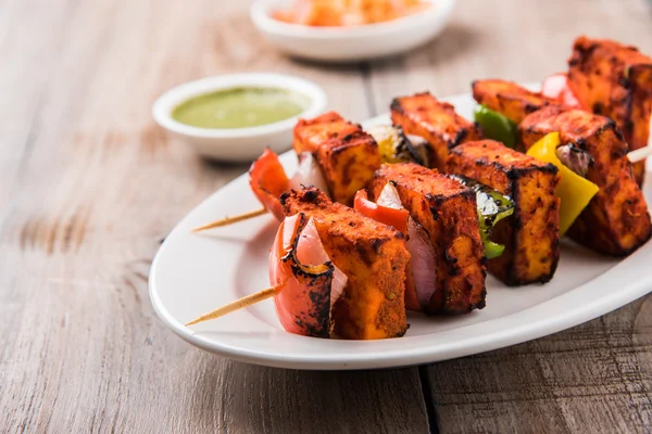 Paneer Tikka Kabab - Hint Tandoori peynir şişleri, malai paneer tikka / biber paneer malai paneer kabab, servis beyaz tabak Barbekü sopa ve renkli kırmızı biber ve soğan, yeşil sos ile