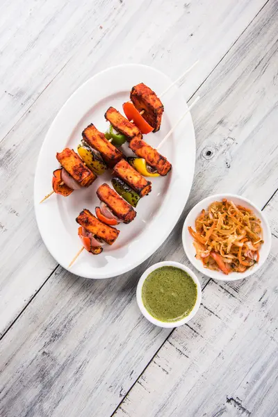 Paneer Tikka Kabab - Tandoori pinchos de queso indio, malai paneer tikka / malai paneer kabab, chile paneer servido en plato blanco con palo de barbacoa y colorido capsicum y cebolla, con salsa verde —  Fotos de Stock