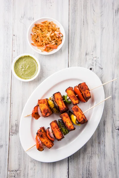 Paneer Tikka Kabab - Tandoori pinchos de queso indio, malai paneer tikka / malai paneer kabab, chile paneer servido en plato blanco con palo de barbacoa y colorido capsicum y cebolla, con salsa verde —  Fotos de Stock