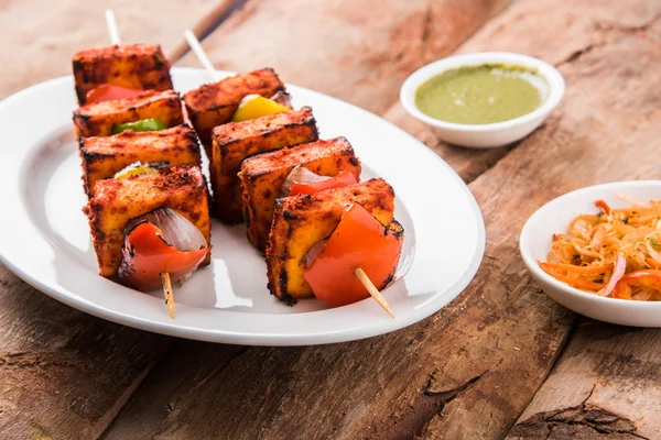 Paneer Tikka Kabab - Tandoori Indian cheese skewers, malai paneer tikka / malai paneer kabab, chilli paneer served in white plate with barbecue stick and colourful capsicum and onion, with green sauce — Stock Photo, Image