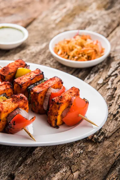 Paneer Tikka Kabab - Tandoori pinchos de queso indio, malai paneer tikka / malai paneer kabab, chile paneer servido en plato blanco con palo de barbacoa y colorido capsicum y cebolla, con salsa verde —  Fotos de Stock