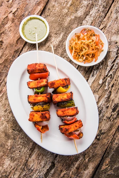 Paneer tikka kabab - indische Tandoori-Käsespieße, malai paneer tikka / malai paneer kabab, Chili paneer serviert in weißem Teller mit Grillspieß und bunten Paprika und Zwiebeln, mit grüner Sauce — Stockfoto