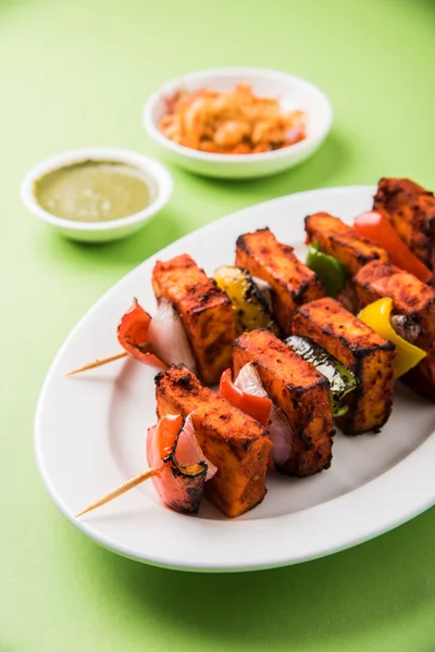 Paneer Tikka Kabab - Tandoori Indian cheese skewers, malai paneer tikka / malai paneer kabab, chilli paneer served in white plate with barbecue stick and colourful capsicum and onion, with green sauce — Stock Photo, Image