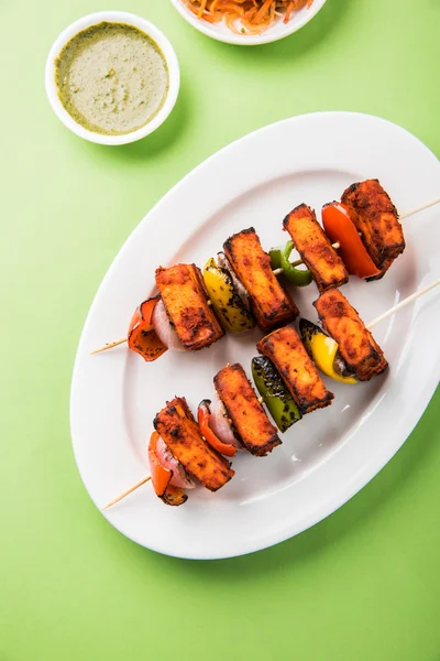 Paneer Tikka Kabab - Tandoori Indian cheese skewers, malai paneer tikka / malai paneer kabab, chilli paneer served in white plate with barbecue stick and colourful capsicum and onion, with green sauce — Stock Photo, Image