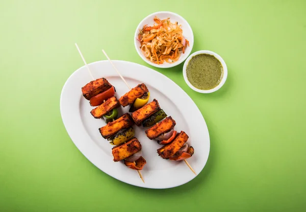 Paneer Tikka Kabab - Tandoori Indian cheese skewers, malai paneer tikka / malai paneer kabab, chilli paneer served in white plate with barbecue stick and colourful capsicum and onion, with green sauce — Stock Photo, Image