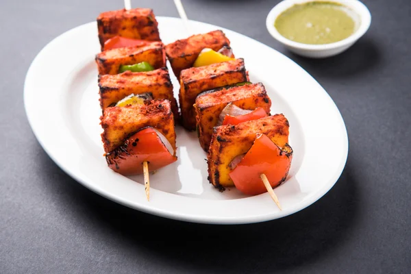 Paneer Tikka Kabab - Tandoori Indian cheese skewers, malai paneer tikka / malai paneer kabab, chilli paneer served in white plate with barbecue stick and colourful capsicum and onion, with green sauce — Stock Photo, Image