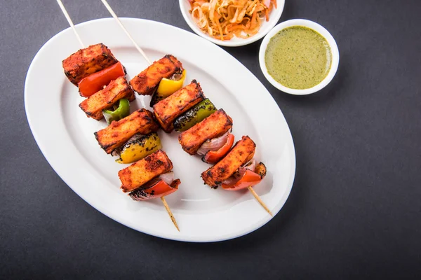 Paneer Tikka Kabab - Tandoori Indian cheese skewers, malai paneer tikka / malai paneer kabab, chilli paneer served in white plate with barbecue stick and colourful capsicum and onion, with green sauce — Stock Photo, Image