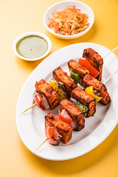 Paneer Tikka Kabab - Tandoori pinchos de queso indio, malai paneer tikka / malai paneer kabab, chile paneer servido en plato blanco con palo de barbacoa y colorido capsicum y cebolla, con salsa verde —  Fotos de Stock