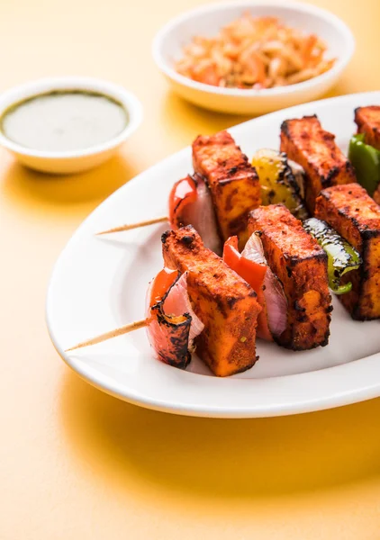 Paneer Tikka Kabab - Tandoori Indian cheese skewers, malai paneer tikka / malai paneer kabab, chilli paneer served in white plate with barbecue stick and colourful capsicum and onion, with green sauce — Stock Photo, Image