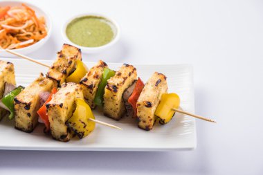 Paneer Tikka Kabab - Hint Tandoori peynir şişleri, malai paneer tikka / biber paneer malai paneer kabab, servis beyaz tabak Barbekü sopa ve yeşil sos, seçici odak ile