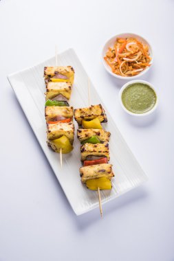 Paneer Tikka Kabab - Hint Tandoori peynir şişleri, malai paneer tikka / biber paneer malai paneer kabab, servis beyaz tabak Barbekü sopa ve yeşil sos, seçici odak ile