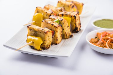 Paneer Tikka Kabab - Hint Tandoori peynir şişleri, malai paneer tikka / biber paneer malai paneer kabab, servis beyaz tabak Barbekü sopa ve yeşil sos, seçici odak ile