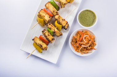 Paneer Tikka Kabab - Hint Tandoori peynir şişleri, malai paneer tikka / biber paneer malai paneer kabab, servis beyaz tabak Barbekü sopa ve yeşil sos, seçici odak ile