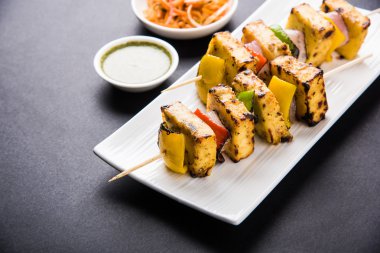 Paneer Tikka Kabab - Hint Tandoori peynir şişleri, malai paneer tikka / biber paneer malai paneer kabab, servis beyaz tabak Barbekü sopa ve yeşil sos, seçici odak ile