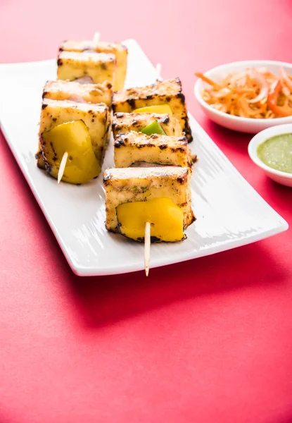 Paneer Tikka Kabab - spiedini di formaggio indiano Tandoori, paneer di malai tikka / malai paneer kabab, paneer di peperoncino servito in piatto bianco con bastone da barbecue e peperoncino colorato e cipolla, con salsa verde — Foto Stock