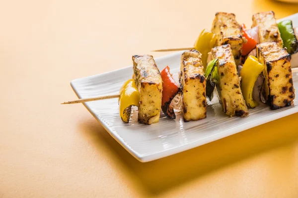 Paneer Tikka Kabab - индийские сырные шашлыки тандури, малай панир тикка / малай панир кабаб, чили панир подается в белой тарелке с палочкой для барбекю и зеленым соусом, избирательный фокус — стоковое фото