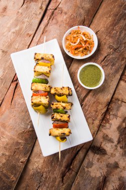 Paneer Tikka Kabab - Hint Tandoori peynir şişleri, malai paneer tikka / biber paneer malai paneer kabab, servis beyaz tabak Barbekü sopa ve yeşil sos, seçici odak ile