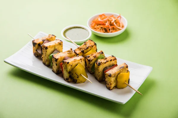 Paneer Tikka Kabab - индийские сырные шашлыки тандури, малай панир тикка / малай панир кабаб, чили панир подается в белой тарелке с палочкой для барбекю и зеленым соусом, избирательный фокус — стоковое фото
