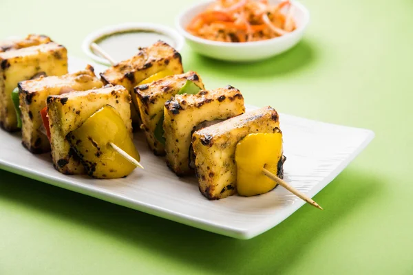 Paneer Tikka Kabab - Tandoori Indian cheese skewers, malai paneer tikka / malai paneer kabab, chilli paneer served in white plate with barbecue stick and green sauce, selective focus — Stock Photo, Image