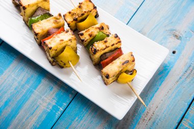 Paneer Tikka Kabab - Hint Tandoori peynir şişleri, malai paneer tikka / biber paneer malai paneer kabab, servis beyaz tabak Barbekü sopa ve yeşil sos, seçici odak ile