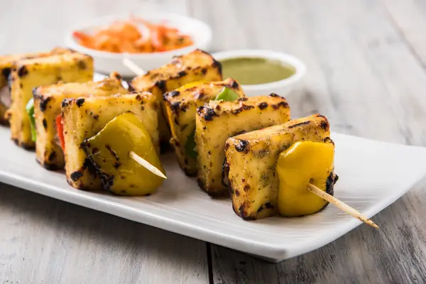 Paneer Tikka Kabab - Espetos de queijo indiano Tandoori, paneer malai tikka / paneer malai kabab, paneer chilli servido em placa branca com pau de churrasco e molho verde, foco seletivo — Fotografia de Stock