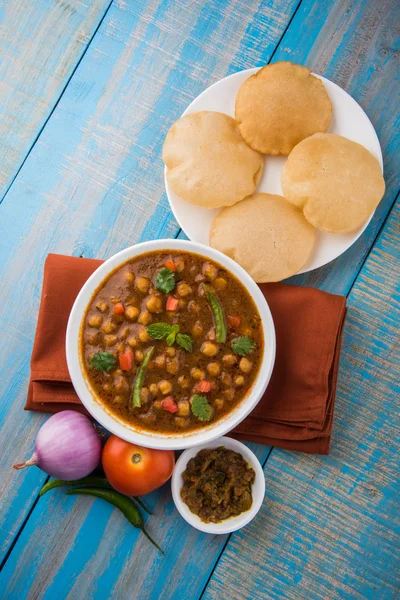 spicy chick peas also known as Chola Masala or Chana Masala or Chole served with fried puri, pickle and green salad