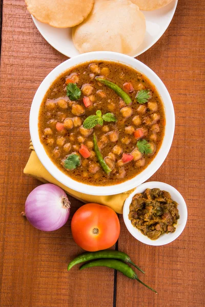 spicy chick peas also known as Chola Masala or Chana Masala or Chole served with fried puri, pickle and green salad