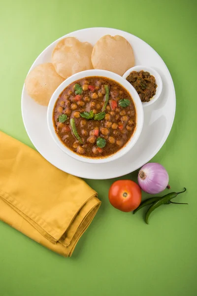 spicy chick peas also known as Chola Masala or Chana Masala or Chole served with fried puri, pickle and green salad
