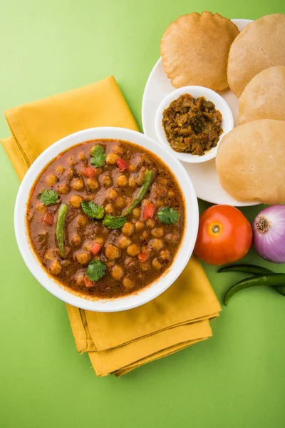 spicy chick peas also known as Chola Masala or Chana Masala or Chole served with fried puri, pickle and green salad