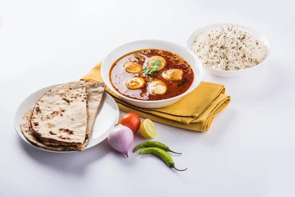 egg curry with roti/chapati and jeera rice, tasty and spicy anda curry with roti and rice, indian egg masala curry served in ceramic bowl with roti, salad and jeera rice