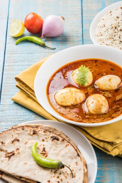 egg curry with roti/chapati and jeera rice, tasty and spicy anda curry with roti and rice, indian egg masala curry served in ceramic bowl with roti, salad and jeera rice