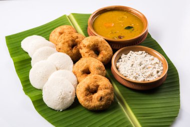 Sambar Vada & Idli ile sambar, hindistan cevizi chutney ve kırmızı domates chutney toprak kaplar, beyaz arka plan üzerinde yeşil muz yaprağı üzerinde servis