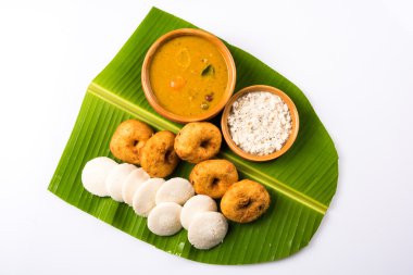 Sambar Vada & Idli ile sambar, hindistan cevizi chutney ve kırmızı domates chutney toprak kaplar, beyaz arka plan üzerinde yeşil muz yaprağı üzerinde servis