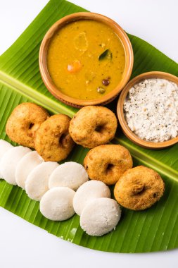 Sambar Vada & Idli ile sambar, hindistan cevizi chutney ve kırmızı domates chutney toprak kaplar, beyaz arka plan üzerinde yeşil muz yaprağı üzerinde servis