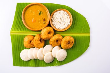 Sambar Vada & Idli ile sambar, hindistan cevizi chutney ve kırmızı domates chutney toprak kaplar, beyaz arka plan üzerinde yeşil muz yaprağı üzerinde servis