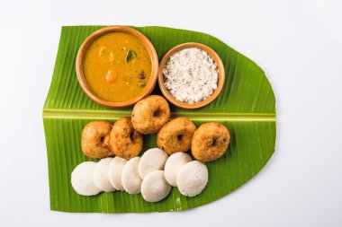 Sambar Vada & Idli ile sambar, hindistan cevizi chutney ve kırmızı domates chutney toprak kaplar, beyaz arka plan üzerinde yeşil muz yaprağı üzerinde servis