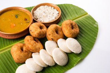 Sambar Vada & Idli ile sambar, hindistan cevizi chutney ve kırmızı domates chutney toprak kaplar, beyaz arka plan üzerinde yeşil muz yaprağı üzerinde servis